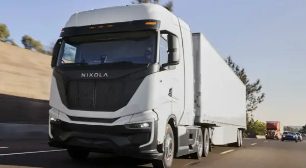 Le Nikola One, un camion blanc futuriste, roule sur l'autoroute sous un ciel bleu clair.