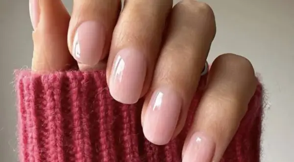 Delikatne, różowe paznokcie w stylu "soap nails" lśnią na tle grubego, różowego swetra.