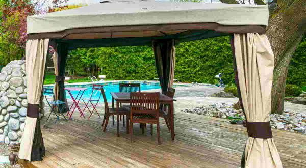 Gazebo su terrazza in legno, con tavolo e sedie, vicino a una piscina. Soluzione per come fissare un gazebo su terrazza senza bucare il pavimento.