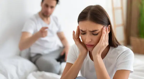 Mujer angustiada, con las manos en la cabeza, mientras su pareja le grita. Siente que mi mujer me maltrata psicológicamente.