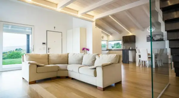 Soggiorno moderno con travi in legno di bianco, divano beige e cucina a vista.