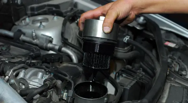 Cambio olio motore: un meccanico rimuove il filtro olio esausto, mostrando dove si trova nel vano motore.