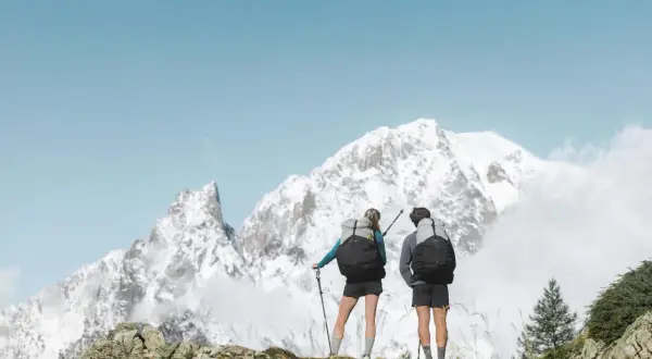 Deux randonneurs, prêts pour une randonnée de 3 jours, contemplent un paysage montagneux enneigé sous un ciel bleu.