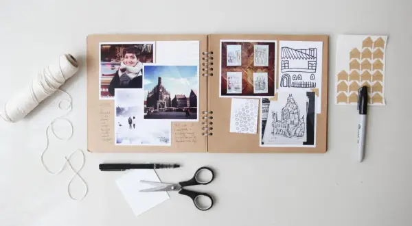 Oto przykład, co to jest scrapbooking: otwarta księga z przyklejonymi zdjęciami, rysunkami i notatkami, obok nożyczki, pisak i sznurek.