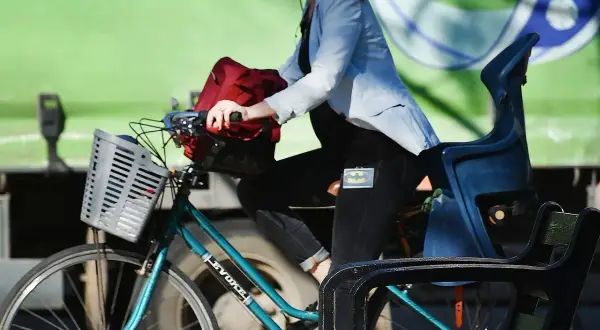 Kobieta w jasnej marynarce i czarnych spodniach z naszywką Batmana jedzie na rowerze. Velo Poprad to jej środek transportu.