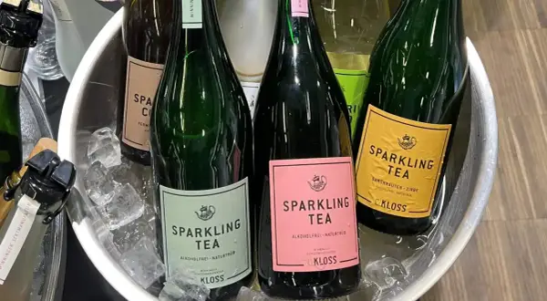 Butelki z napojem typu wino cava, schłodzone w lodzie. Etykiety w kolorach zielonym, różowym i żółtym, z napisem "Sparkling Tea".