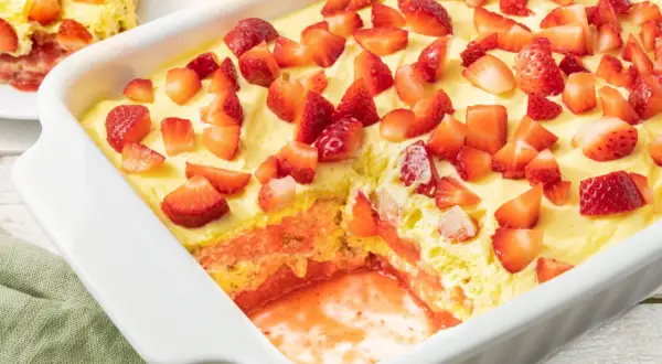 Tiramisù fragole in una teglia bianca, con strati di crema, biscotti e tante fragole fresche a pezzi.