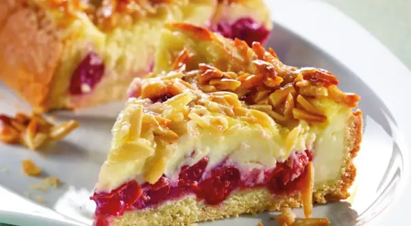 Ein Stück von Omas Kirschkuchen mit Pudding, belegt mit Mandelblättchen. Saftige Kirschen und cremiger Pudding unter knuspriger Kruste.