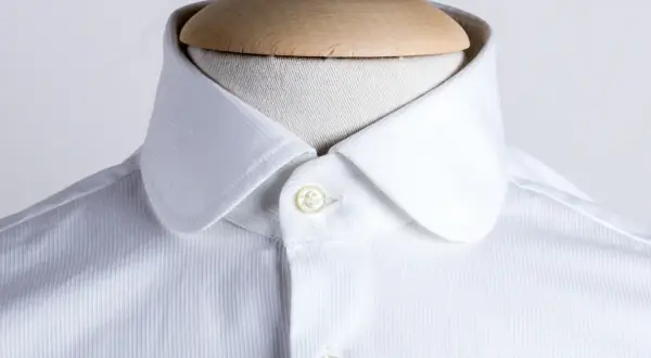 Dettaglio di una camicia bianca con colletto arrotondato, uno dei tanti tipi di colletto camicia, su un manichino.