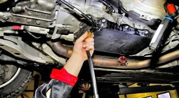 Mechanik wykonuje wymianę oleju w skrzyni automatycznej, podłączając wężyk do układu.