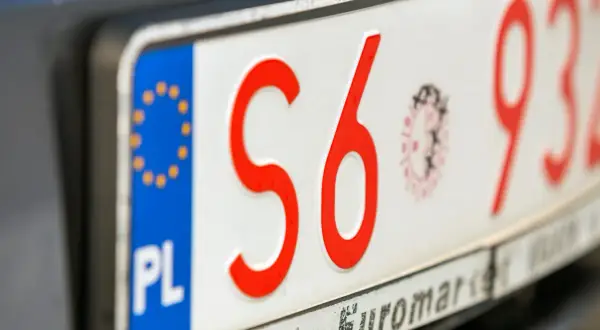 Zbliżenie na polskie tablice rejestracyjne z czerwonymi znakami. Widoczne litery "S6" i cyfry "932".