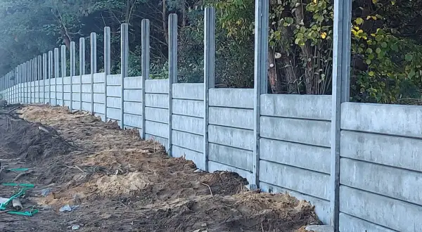 Wykończenie słupów zewnętrznych w postaci betonowego muru oporowego, budowanego z prefabrykowanych elementów, z widocznym terenem budowy.