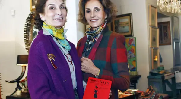 Naty Abascal y otra mujer posan con un libro rojo titulado "100% NATY".