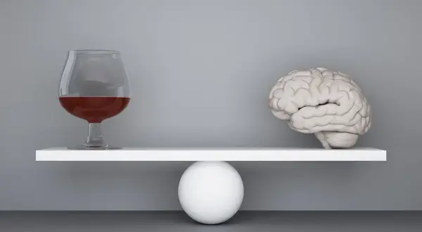 Szalka wagi z mózgiem przechyla się, gdy obok pojawia się kieliszek z alkoholem, symbolizując zmianę zachowania po alkoholu.