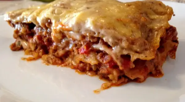 Kawałek zapieczonej lasagne z ciągnącym się serem na białym talerzu.