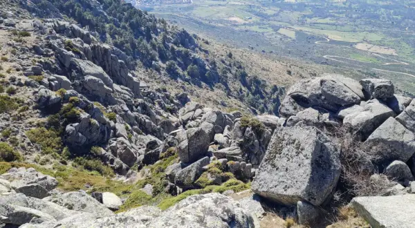 Rocas y vegetación en el cancho del águila, con un valle verde y camino serpenteante al fondo.