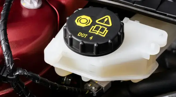Le réservoir de liquide de frein est visible, avec le bouchon noir marqué "DOT 4". Le niveau du liquide est bien visible dans le récipient translucide.