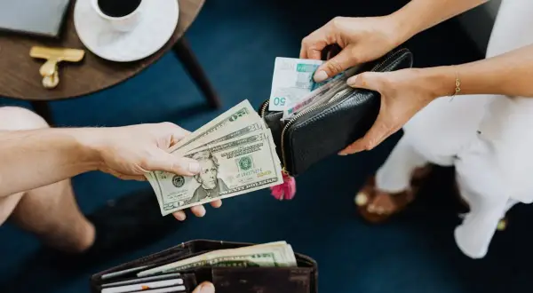 Dwie osoby wymieniają się pieniędzmi. Jedna trzyma dolary, druga wkłada do portfela banknoty. Co lepiej zabrać do Turcji euro czy dolary?