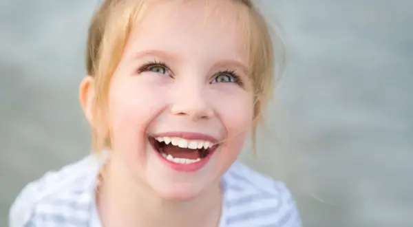 Uśmiechnięta dziewczynka z blond włosami, której radość przypomina o sile ducha w walce z zespołem Angelmana.