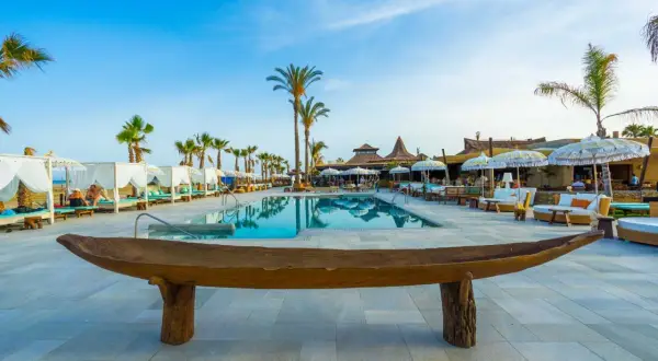 Un lujoso beach club en Mojácar con piscina, palmeras y cabañas blancas.