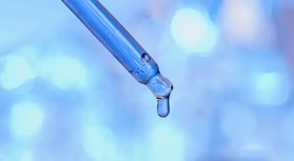 Kropla błękitnego serum, zawierającego peptyd miedziowy, spływa z pipety na rozmyte, błękitne tło.