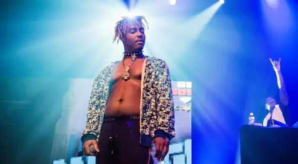 Juice WRLD on stage, a testament to his massive Juice WRLD Spotify streams. The artist, bathed in blue light, holds a microphone and a bottle.