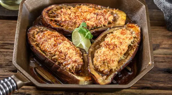 Berenjena airfryer rellena y gratinada, servida en una sartén de hierro fundido con un toque de lima.