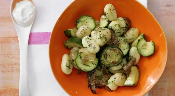 Gnocchi mit Zucchini und Pilzen in einer orangen Schüssel, dazu ein Löffel cremiger Dip. Eine köstliche zucchini pfanne.