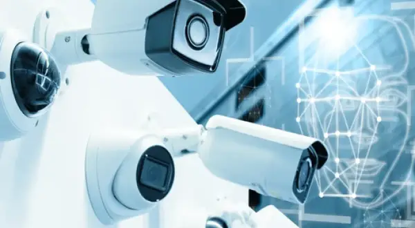 Plusieurs caméras de surveillance sont montées sur un mur blanc. En arrière-plan, un visage stylisé avec des points connectés suggère la technologie de caméra ai.