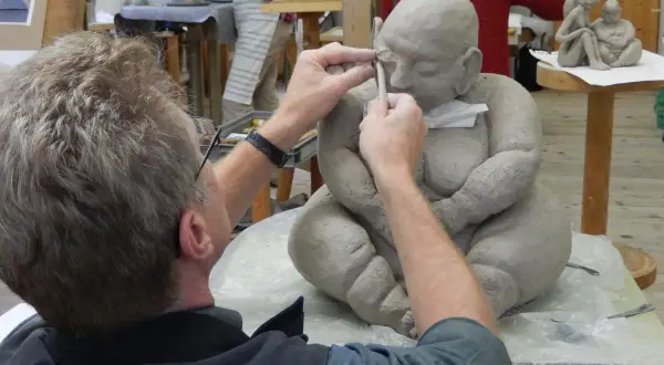 Ein Künstler formt mit Werkzeug eine Tonfigur in einem Atelier.