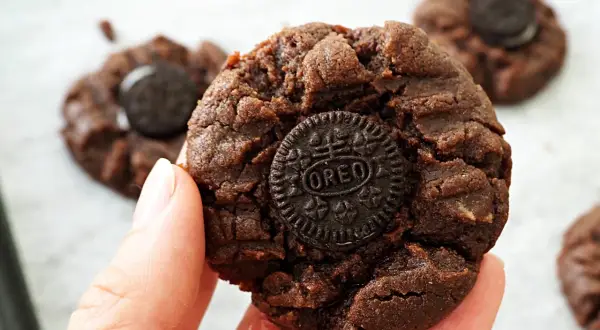 En hand håller en chokladkaka med en Oreo-kaka i mitten. Flera liknande nutella kakor syns i bakgrunden.