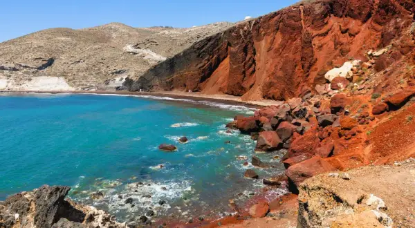Santorini plaże: turkusowe morze obmywa czerwoną, wulkaniczną plażę, otoczoną skalistymi klifami.