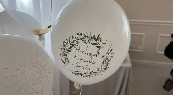 Białe balony z napisem "Pierwsza Komunia Święta" i motywem gołębicy oraz kielicha z hostią.