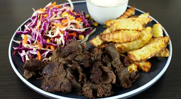 Talerz z mięsem kebab, frytkami, surówką z czerwonej kapusty i sosem.