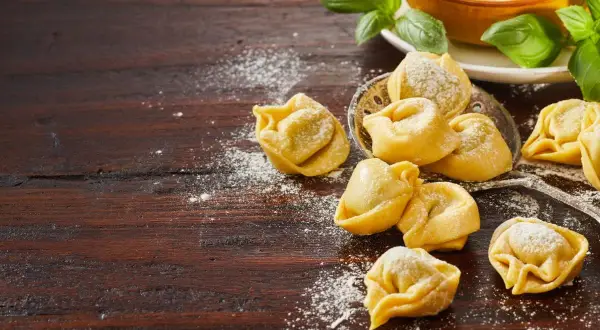 Pyszne tortellini na obiad, posypane mąką, obok świeżej bazylii i kulek mozzarelli.