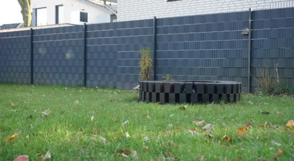 Moderne Zaun-Sichtschutz-Ideen: Dunkelgrauer Lamellenzaun mit dekorativem Feuerring im Garten.