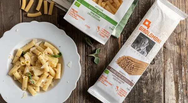 Piatto di maccheroni conditi e pacchi di pasta della Gino Girolomoni Cooperativa Agricola, con grano italiano.