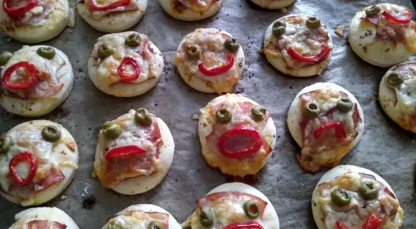 Lustige kleine Pizzen mit Olivenaugen und Paprikamund, perfekt zum glutenfrei essen.