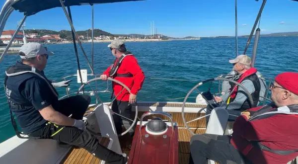 Uomini imparano a navigare durante un corso skipper, con un istruttore che guida il timone.