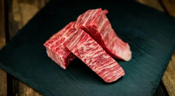 Drei Stücke erstklassiges Kobe Rindfleisch mit feiner Marmorierung liegen auf einem dunklen Stein.