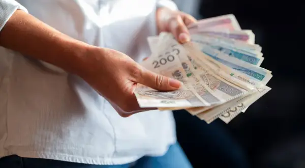 Ręce trzymające polskie banknoty. Zastanawiasz się, jaka będzie najniższa krajowa 2025 i ile na rękę dostaniesz?