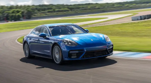 Niebieski Porsche Panamera GTS pokonuje zakręt na torze wyścigowym, z zielonymi wzgórzami w tle.