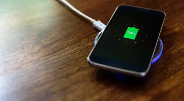 Smartfon na drewnianym blacie, wskaźnik pokazuje 100% – zakończone ładowanie baterii.