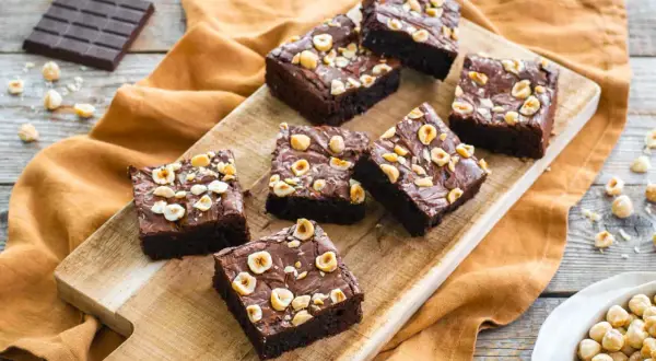Deliziosi brownies senza glutine con nocciole tostate, disposti su un tagliere di legno.