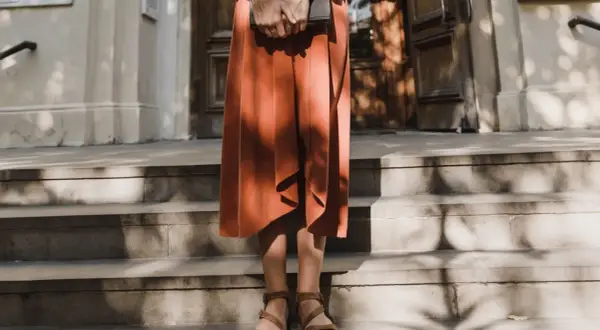 Kobieta w pomarańczowej sukience i sandałach trzyma książkę. Stylizacja idealna do letniego lookbooka.