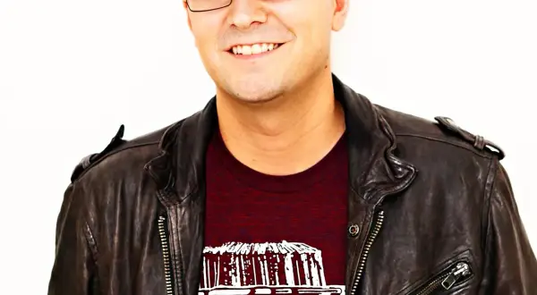 A smiling man in a leather jacket and cap, possibly inspired by the creative spirit behind Luke Laird songs.