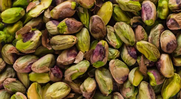 Un primo piano di pistacchi sgusciati, con sfumature verdi e violacee, pronti per essere gustati. Questi frutti secchi provengono da un **maggior produttore di pistacchi**.