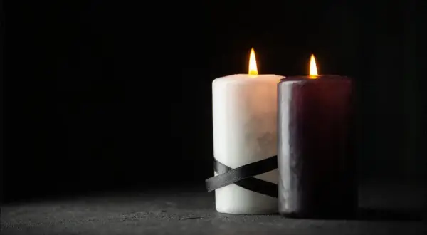 Dwie płonące świece, biała z czarną wstążką i ciemna, symbolizują patologiczną żałobę, która nie ustępuje.