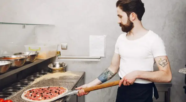 Pizzaiolo con barba prepara una pizza con farina per pizza 0 o 00.