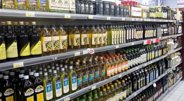 Scaffali di un supermercato pieni di bottiglie di olio d'oliva. Quante olive per un litro di olio? La risposta è nella varietà di marche e formati.